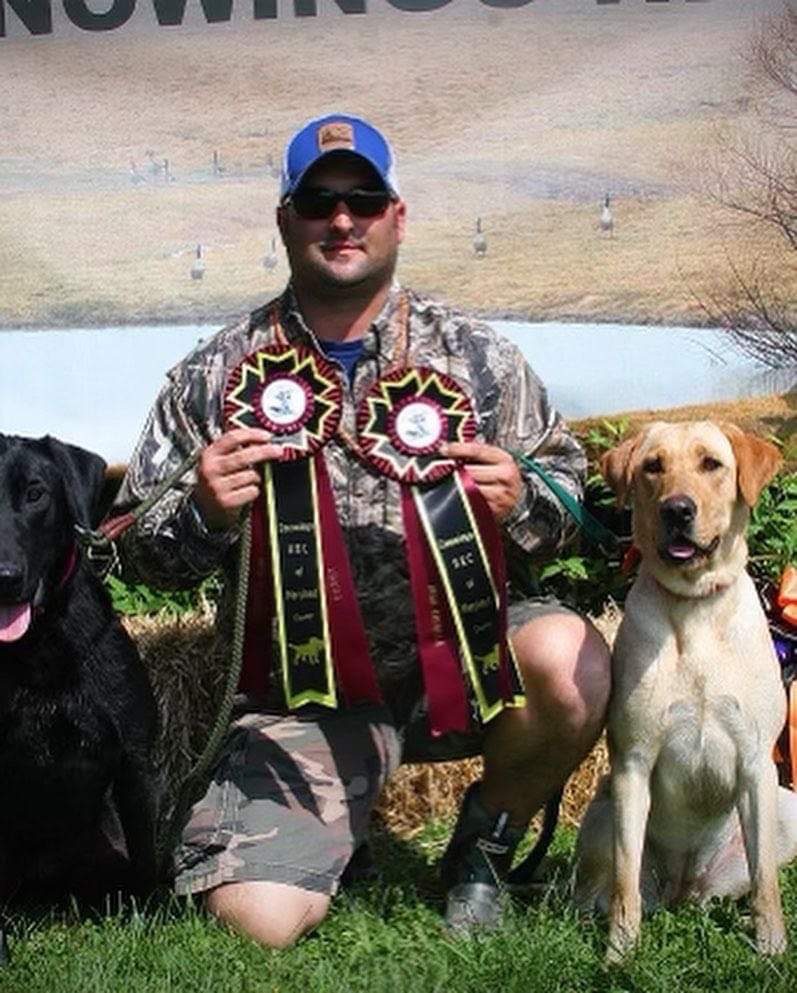 A man holding two awards and three dogs.